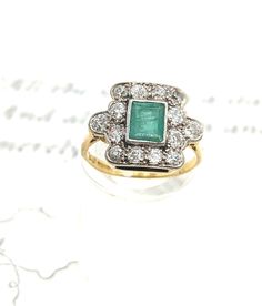 Stunning Vintage Emerald and Diamond Cocktail Ring - 18ct Hallmarked Yellow Gold Embrace timeless elegance with this breathtaking Edwardian style vintage cocktail ring. This exquisite piece features a captivating square cluster design showcasing 14 natural diamonds and a central square cut emerald, radiating a rich, verdant hue. The centrepiece Emerald is surrounded by a dazzling halo of diamonds, adding a touch of brilliance and luxury. Crafted from lustrous 18ct yellow gold, this ring is not o Classic Cluster Emerald Ring, Art Deco Yellow Gold Emerald Ring With Brilliant Cut, Vintage Emerald Ring In Yellow Gold With Brilliant Cut, Classic Emerald Ring With Prong Setting In Cluster Shape, Vintage Green Diamond Ring With Halo Setting, Classic Cluster Emerald Ring With Prong Setting, Antique Yellow Gold Cluster Ring With Halo Setting, Green Vintage Diamond Ring With Halo Setting, Green Diamond Ring With Halo Setting In Vintage Style