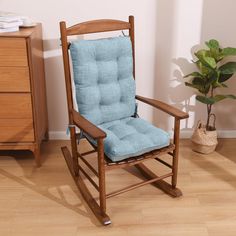 a wooden rocking chair with blue cushions in a room next to a potted plant