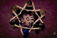 four women are sitting in a circle on the floor with their hands together and looking down at them