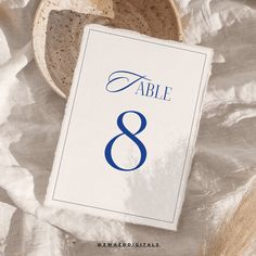 a table number is placed next to a bowl on a white sheet with blue lettering