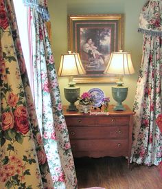 a bedroom with floral curtains and a painting hanging on the wall above an old dresser