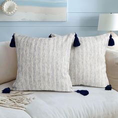 two white pillows with blue tassels sit on a couch in front of a painting