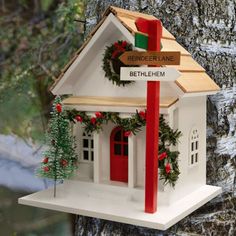 a white birdhouse with a red ribbon hanging from it's roof next to a tree