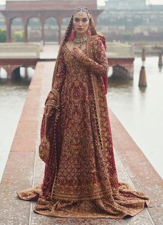 a woman in a red and gold bridal gown standing on a walkway next to water