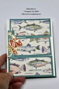 a hand holding a card with fish on it and the words happy birthday written in gold