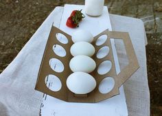 an egg tray with eggs and strawberries sitting on a white tablecloth covered table