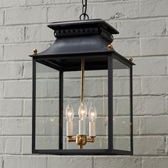 a lantern hanging from the ceiling with three lit candles in front of a brick wall