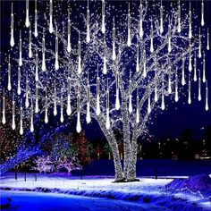 a large tree with many lights hanging from it's branches in the snow at night