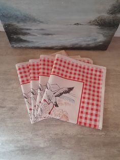 three red and white checkered paper napkins on a table with a painting in the background