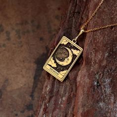 a gold necklace with an image of the moon and stars on it hanging from a rock