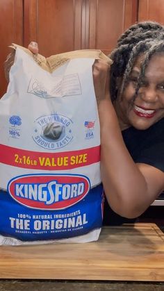 a woman holding up a bag of king'sford the original flour on top of a wooden cutting board