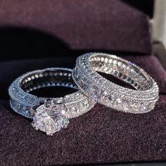 two diamond wedding rings sitting on top of a purple velvet cushion in front of a window