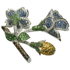 Colored stone and diamond custom brooch in 18k white gold. Tests 18k and weighs 23 grams. There is 7.25 total carats of round brilliant cut diamonds, G color, VS to Si clarity. The other stones are natural yellow sapphires, green tsavorite and natural blue sapphires. Measures 2" x 2" Condition is new. Brooch Ideas, Diamond Flower Brooch, Titanic Jewelry, Sparkly Accessories, Jewelry Design Drawing, Gold Brooch, Color Stones, Colored Stone, Diamond Brooch