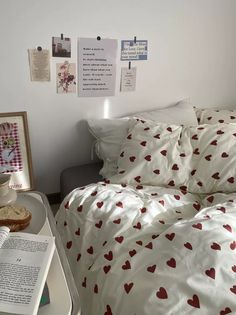 a bed with red hearts on it next to a book and some pictures hanging on the wall