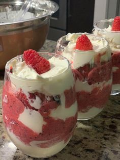 three desserts with raspberries and whipped cream in glasses sitting on a counter