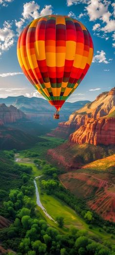 a hot air balloon flying over a valley in the mountains with green grass and trees