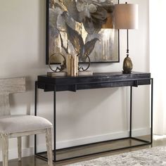 a black console table with two lamps and a painting on the wall in front of it