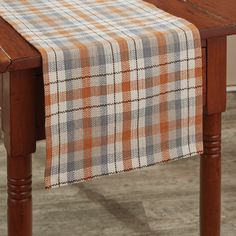 an orange and white plaid table runner on top of a wooden table with wood legs