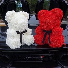 two teddy bears are sitting on the hood of a car, one red and one white