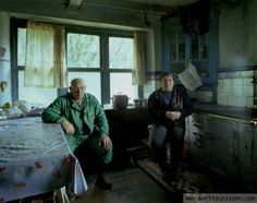 a man and woman sitting at a table in an old kitchen