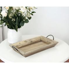 a wooden tray sitting on top of a white table next to a vase with flowers