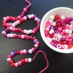 a bowl filled with beads next to a pink and white bead necklace on a table