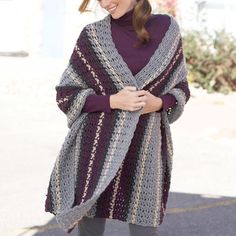 a woman wearing a purple and gray crocheted ponchy with her hands in her pockets