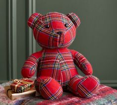 a red teddy bear sitting on top of a bed next to a small gift box