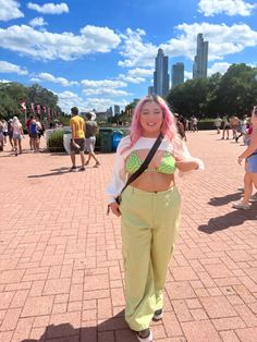 a woman with pink hair and green pants standing in the middle of a brick walkway