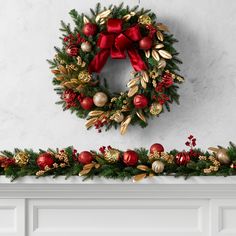 a christmas wreath with red and gold ornaments hanging on the mantle next to a fireplace