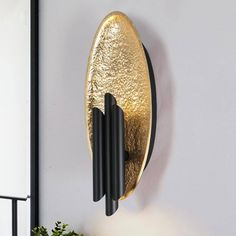 a gold and black clock mounted to the side of a wall next to a potted plant