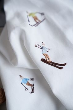 two white sheets with skiers on them and one has a brown teddy bear in the corner