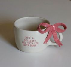 a coffee cup with a pink bow on the side and saying she's a designer and that's her super power