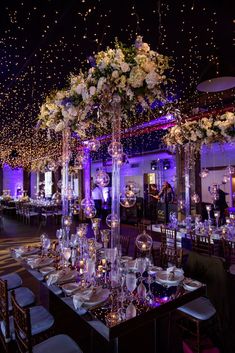 the tables are set for an event with white flowers and candles in tall vases