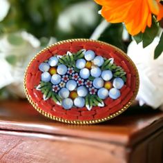 Discover our enchanting vintage Italian mosaic oval brooch from the 1960s. This brooch is a testament to the rich heritage of Italian mosaic jewelry. 🌼 It features a design of delicate white and blue flowers elegantly framed by a vibrant orange mosaic background. The intricate details of the mosaic bring to life the essence of Italian craftsmanship. 🌞 Encased in an oval gold tone frame, this brooch is a wearable work of art that effortlessly blends vintage charm with vibrant color. 🎨The art of mosaic dates back to the Roman Empire. Micro mosaic jewelry became popular in the 17th - 19th centuries as rich European families were touring Europe especially Italy. Italian craftsmen turned their glass making skills into the production of micro mosaic jewelry for their rich visitors. In Italy, Heirloom Oval Brooches As Gift, Heirloom Oval Brooches For Gifts, Handmade Victorian Oval Brooches, Vintage Handmade Brooches For Gifts, Vintage Oval Brooches For Collectors, Vintage Oval Brooches For Wedding, Handmade Vintage Brooch For Anniversary, Handmade Vintage Brooches For Anniversary, Vintage Oval Wedding Brooches