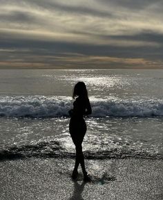 a woman standing on top of a beach next to the ocean under a cloudy sky