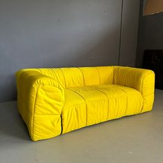 a yellow couch sitting on top of a white floor next to a lamp and wall