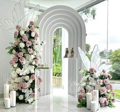 flowers and candles are arranged on the floor in front of an arch with angel wings