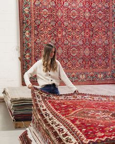 a woman standing next to a pile of rugs