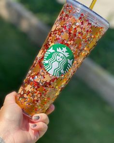 a person holding up a starbucks cup with gold flakes and a straw in it