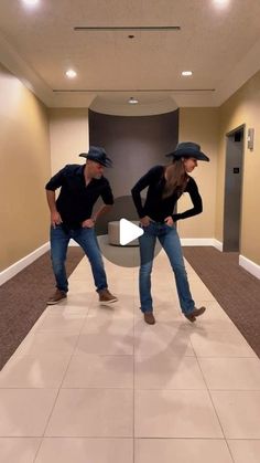 two people wearing hats and jeans standing in an empty room