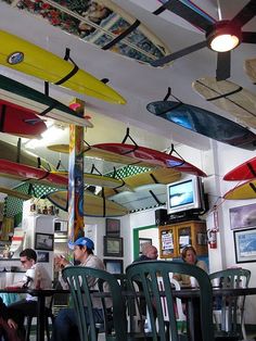 people sitting at tables in a restaurant with surfboards hanging from the ceiling above them