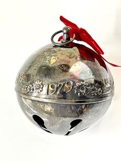 a silver bell ornament with red ribbon hanging from it's side on a white background