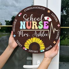 two hands holding up a wooden sign that says school nurse and mrs ashle with sunflowers