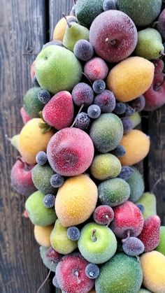 a bunch of fruit hanging from the side of a wooden wall with berries and apples on it