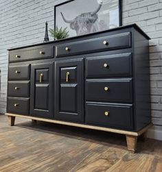 a black dresser with gold handles and knobs on it's drawers in front of a brick wall