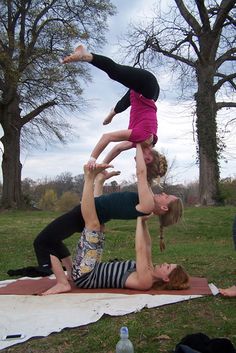 two women doing handstands on a blanket in the grass with trees behind them