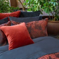 a bed covered in red and blue pillows next to a potted plant on top of a table