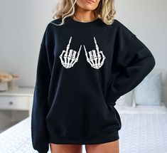 Rock On Skeleton Hands Sweatshirt, Halloween Sweatshirt, Halloween Skeleton Hand Sweatshirt, Skeleton Sweatshirt, Skeleton Hands Sweatshirt Hi! Welcome to✨Northstar ✨ ✨As the weather gets colder, you want clothes that keep you and your body warm. Here, Northstar  is ready to keep you warm with its unique designs..✨ ✨Product Features✨ 👉Medium-heavy fabric (8.0 oz/yd² (271.25 g/m 👉Loose fit 👉Runs true to size 👉50% cotton, 50% polyester 👉Tear-away label ✨Care Instructions✨ 👉Wash item inside out in cold water, do not bleach, do not dry clean, do not iron directly on the design. ✨How To Order✨ 👉 First, please review all photos and make sure you read the descriptions. 1- Choose your size and color from the drop-down menus. 2- If you have personalization, enter the necessary information in Winter Skull Print Relaxed Fit Tops, Edgy Oversized Tops For Halloween, Relaxed Fit Skull Print Tops For Winter, Trendy Long Sleeve Tops With Skull Print, Skull Print Relaxed Fit Long Sleeve T-shirt, Edgy Skull Print Sweatshirt For Fall, Fall Skull Print Crew Neck Top, Rock On Skeleton, Halloween Skeleton Hand