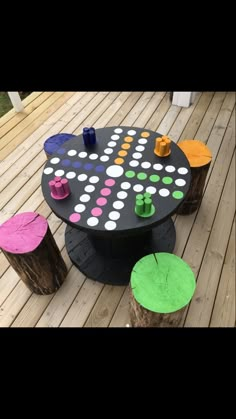 an outdoor table made out of logs and painted with different colors on the top, sitting on a wooden deck